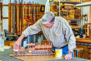 Older man varnishing wooden train in woodshop