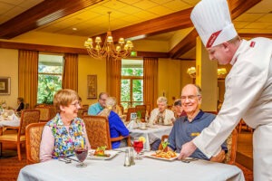 Couple sitting at table in restaurant being served food by chef